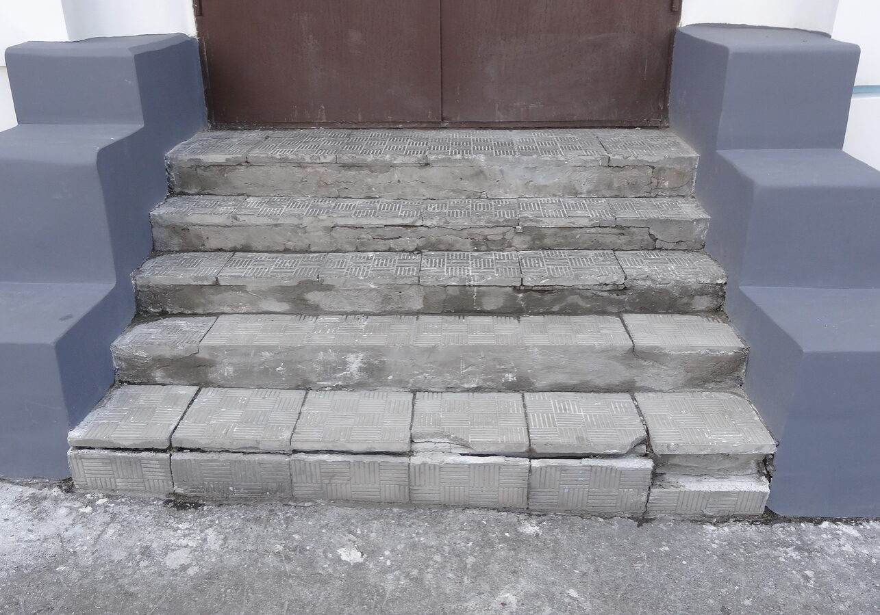 Old stone gray steps with wear marks of destruction with scratches and cracks. Entrance to the street in the shop in the old part of the city.