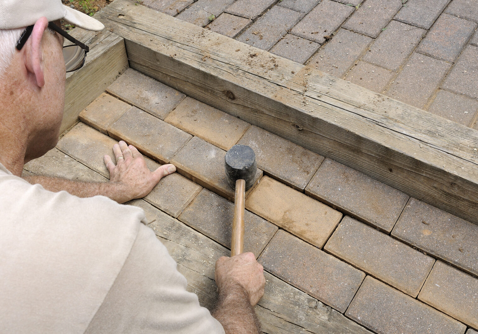 Construction worker installing brick pavers on walkway and steps.